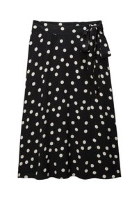 Jupe noire à pois blancs, avec une taille nouée et un design fluide. Texture lisse, coupe mi-longue.