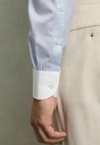 Lichtblauw overhemd met een witte, contrasterende manchette en twee knopen. Glad textuur van de stof, fitted ontwerp, close-up van de mouw en hand.