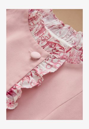 Nærbillede af et rosa stykke tøj med en stofbetrukket knap og blomstret flæsekant i hvidt og rosa omkring halsudskæringen.