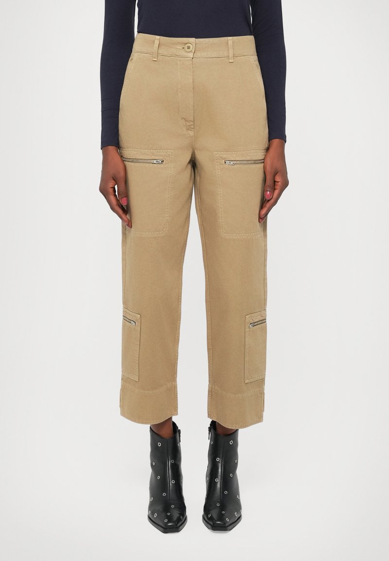 Pantaloni cargo bej cu două buzunare frontale cu fermoar, patch-uri laterale și lungime scurtă. Purtați cu botine negre cu toc, cu accente metalice.