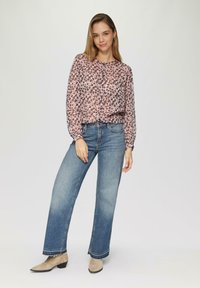 Vloeiende roze blouse met zwart en paars bloemmotief, gecombineerd met blauwe wijdne pantalon en beige enkellaarsjes. Eenvoudig knoopdetail op de blouse.