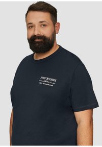 T-shirt bleu marine avec un motif sur le devant comprenant un texte blanc qui dit "FISH 'N CHIPS" et des coordonnées ; manches courtes et col rond.