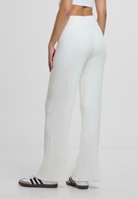 Weiße gerippte Strickhosen mit einem ausgestellten Design und hohem Bund, weicher Textur und kombiniert mit schwarz-weißen Sportschuhen.