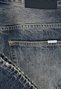 Jeans van denim in een donkere blauwe kleur, met vervaagde delen, gele stiksels en een zwart etiket met reliëftekst op de tailleband.