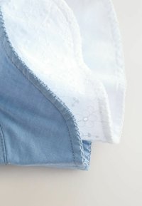 Denimstof met een lichtblauwe tint heeft een witte kanten overlay met bloemige patronen langs de rand. Gestikte zooms overal.