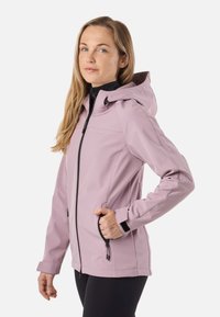 Woman wearing a light purple hooded jacket with black zipper and pockets, standing sideways with one hand in pocket against white background.