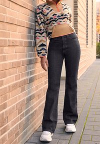 Polaire à enfiler avec un motif géométrique coloré et une fermeture éclair, associée à un jean noir taille haute et des baskets blanches. Texture confortable et douillette.