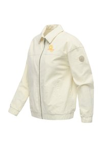 Veste zippée de couleur crème avec col, poignets élastiques, poches avant, logo soleil et vague sur la poitrine, et écusson circulaire sur la manche.
