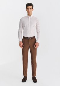 Biała koszula w małe kropki, długie rękawy, klasyczny kołnierzyk; w zestawieniu z brązowymi spodniami i brązowymi butami. Brązowy pasek z srebrną klamrą.