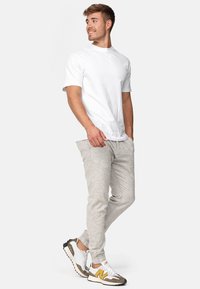 Camiseta blanca de cuello redondo, pantalones ajustados en gris claro y zapatillas multicolores. Ajuste casual. Tela suave con una textura sutil en los pantalones.