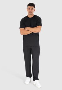 Sort kortærmet t-shirt parret med løse sorte bukser og hvide sneakers, stående positur, enkel design, glat tekstur, afslappet pasform.