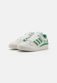 White sneakers with green accents, leather and textile materials, round toe, perforated detailing, and a textured rubber sole.