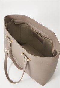 Light taupe leather tote bag with gold hardware, smooth texture, spacious interior, and a zip pocket. Features two sturdy handles.