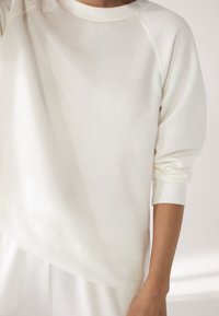 Witte sweatshirt met een ontspannen pasvorm, raglanmouwen en geribde manchetten. De stof heeft een gladde textuur en minimale stikdetails.