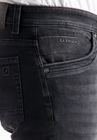 Tume denimist valmistatud teksad, millel on reguleeritud disain, tagaküljel tasku, millel on kiri "Gabbiano", hõbedased tarvikud ja tekstureeritud kangas.