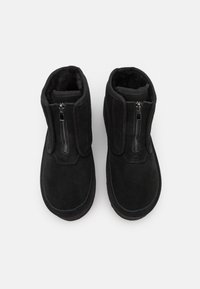 Botine negre din suede cu o textură netedă, dotate cu un fermoar lateral și detalii elastice pentru o purtare ușoară. Formă simplă, cu vârf rotunjit.