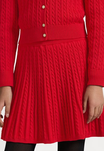 Σετ κόκκινο πλεκτό πουλόβερ και φούστα με σχέδιο καλώδιο, ριμπ λεπτομέρειες και κουμπιά. Η φούστα είναι plissee για επιπλέον υφή.