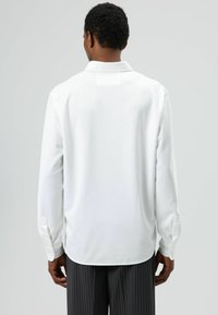 Langärmeliges, weißes Hemd mit Kragen, glatter Textur und Manschetten mit Knöpfen, kombiniert mit Nadelstreifenhosen. Rückansicht gezeigt.