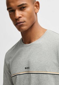 Gray short-sleeve T-shirt with round neck, featuring a black "BOSS" logo and horizontal stripes in gold and black across the chest.