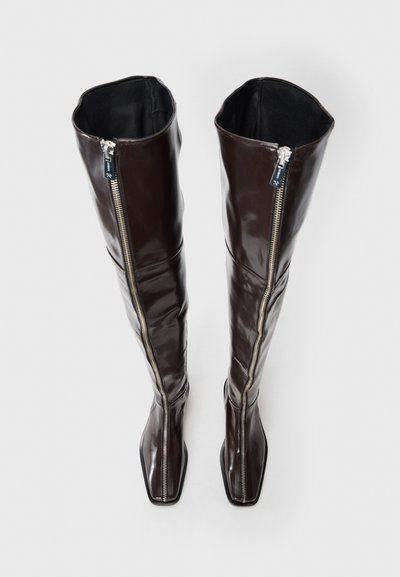 Braune, glänzende Overknee-Stiefel mit quadratischer Schuhspitze, ausgestattet mit einem durchgehenden Reißverschluss an der Außenseite und einer glatten Innenauskleidung.