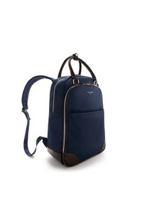 Navy blue backpack with a smooth material, brown leather accents, dual zip closure, and adjustable straps. Features a front pocket.