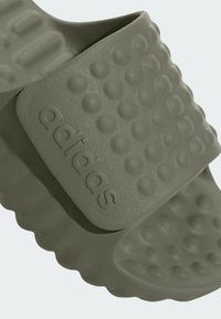 Zelené šľapky Adidas s textúrovaným vrchom, ktorý má vyvýšené body a logo značky. Mäkko, flexibilný materiál a zakrivené okraje.