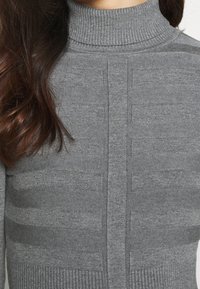 Pull à col roulé gris présentant un motif texturé avec des rayures horizontales alternées et des accents côtelés à l'ourlet et au col.