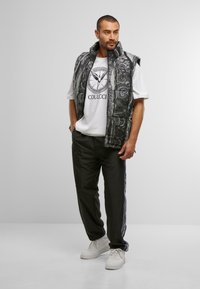 Gilet matelassé à motif noir et blanc sur un t-shirt blanc avec un graphique, associé à un pantalon de jogging noir et des baskets blanches.