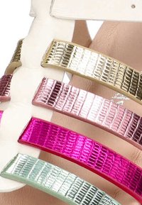 La sandalia multicolor presenta tiras metálicas en dorado, rosa y verde, con un patrón texturizado, sobre una base lisa color crema.