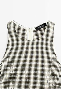 Haut sans manches à rayures verticales noires et blanches avec une fermeture éclair au dos et une étiquette visible de la marque Massimo Dutti près de l'encolure.