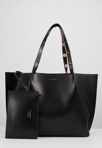 Sac cabas en cuir noir avec clous dorés sur les anses et pochette assortie zippée, tous deux estampillés du logo « Coccinelle ».