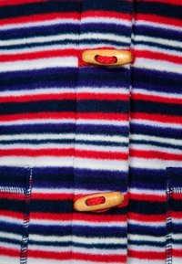 Fleece jacket s červenými, bílými a námořnickými pruhy, s dřevěnými uzávěry a červenými šňůrami. Měkká textura s viditelným prošíváním.