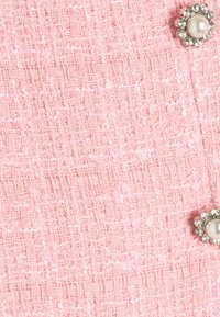 Rosa texturerad tyg med vävda mönster; har en dekorativ knapp med en pärlcentra omgiven av rhinestones.