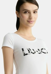 T-shirt bianca a maniche corte con un grande logo in bianco e nero "LIU-JO" e accenti circolari, realizzata in un tessuto liscio e elastico.
