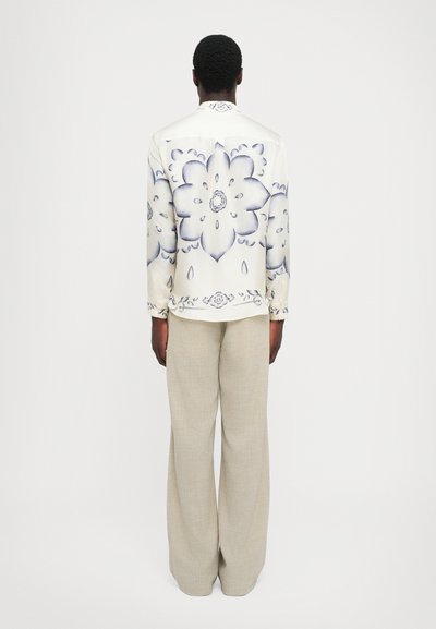 Valkoinen paita kukkakuviolla ja sinisillä yksityiskohdilla, napitettava malli, pitkät hihat; yhdistetty kevyisiin beigeihin leveälahkeisiin housuihin.