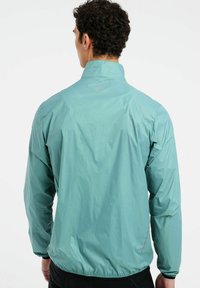 Lengvas, mėtinių žalių spalvų švarkelis su aukštu apykakle, elastinėmis rankogaliais ir surinkta liemene, turintis subtilų logotipo detalę ant nugaros.