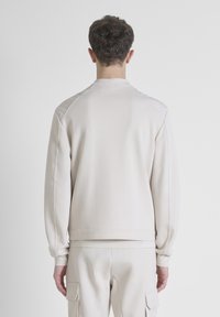 Sudadera de color beige claro en una tela suave, con un cuello redondo y puños acanalados. Diseño limpio sin logotipos ni patrones visibles.