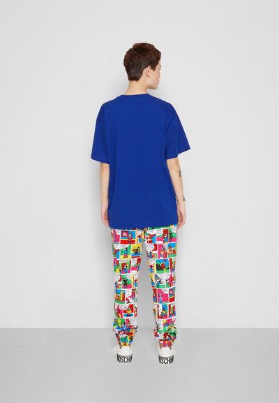 T-shirt azul oversized com mangas curtas, emparelhada com calças coloridas com impressão de banda desenhada apresentando vários painéis, punhos elásticos e ténis brancos.