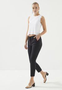 Witte geribbelde mouwloze top gecombineerd met zwarte slim-fit broek, met zijzakken en transparante block-heeled sandalen. Eenvoudig, modern ontwerp.