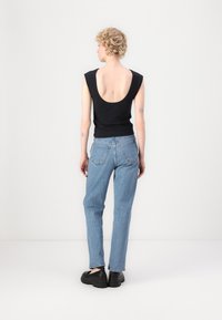 Haut sans manches noir avec un décolleté profond dans le dos, associé à un jean droit bleu clair et des chaussures noires à enfiler.