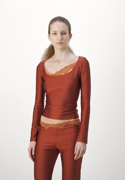 Langsleeve, roestkleurig top met een brede halslijn, voorzien van een oranje kanten rand. Gecombineerd met bijpassende broek met een kanten tailleband.