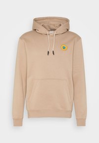 Beige luvtröja med huva, framficka, dragsko i huvan och en liten rund patch med en blå jordglob mot gul bakgrund på bröstet.