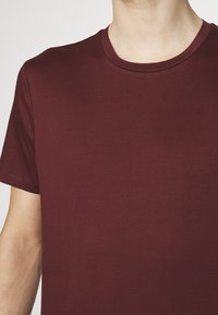 Burgundská bavlněná tričko s kulatým výstřihem a krátkými rukávy, hladká textura a bez viditelných vzorů či kovových detailů.