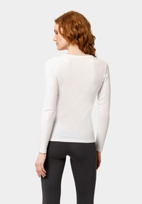 Witte lange mouwtop met een gladde textuur, ronde hals en aansluitende silhoutte, gecombineerd met donkere leggings. Strak, minimalistisch ontwerp.