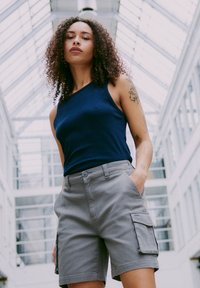 Canotta a coste blu navy abbinata a pantaloni cargo grigi con tasche laterali. Tessuto morbido con una vestibilità confortevole e un design aderente.