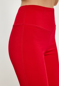 Rote hoch-taillierte Leggings aus glattem, dehnbarem Material mit Flachnähten für Haltbarkeit und Komfort.