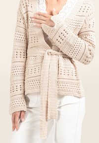 Beige Strickjacke mit offenem Vorderteil, strukturiertem Stoff, langen Ärmeln und einem gebundenen Gürtel in der Taille. Mit einer dekorativen Spitzenborte.
