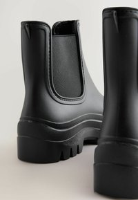 Schwarze Gummi-Regenstiefel mit strukturierten Einsätzen, einer dicken, gerippten Sohle und einer runden Zehenpartie. Das Obermaterial hat elastische Einsätze für ein einfaches Anziehen.