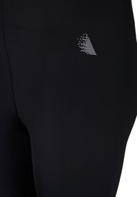 Schwarze sportliche Leggings mit glatter Textur und tailliertem Design, auf dem Oberschenkel mit einem kleinen weißen geometrischen Logo versehen.