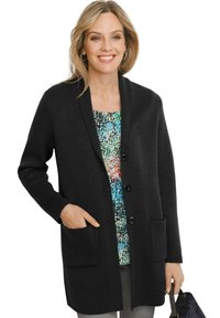 Schwarze Strickjacke mit einem Schalkragen, vorderen Knöpfen und zwei aufgesetzten Taschen. Über einem gemusterten Oberteil in verschiedenen Farben getragen.